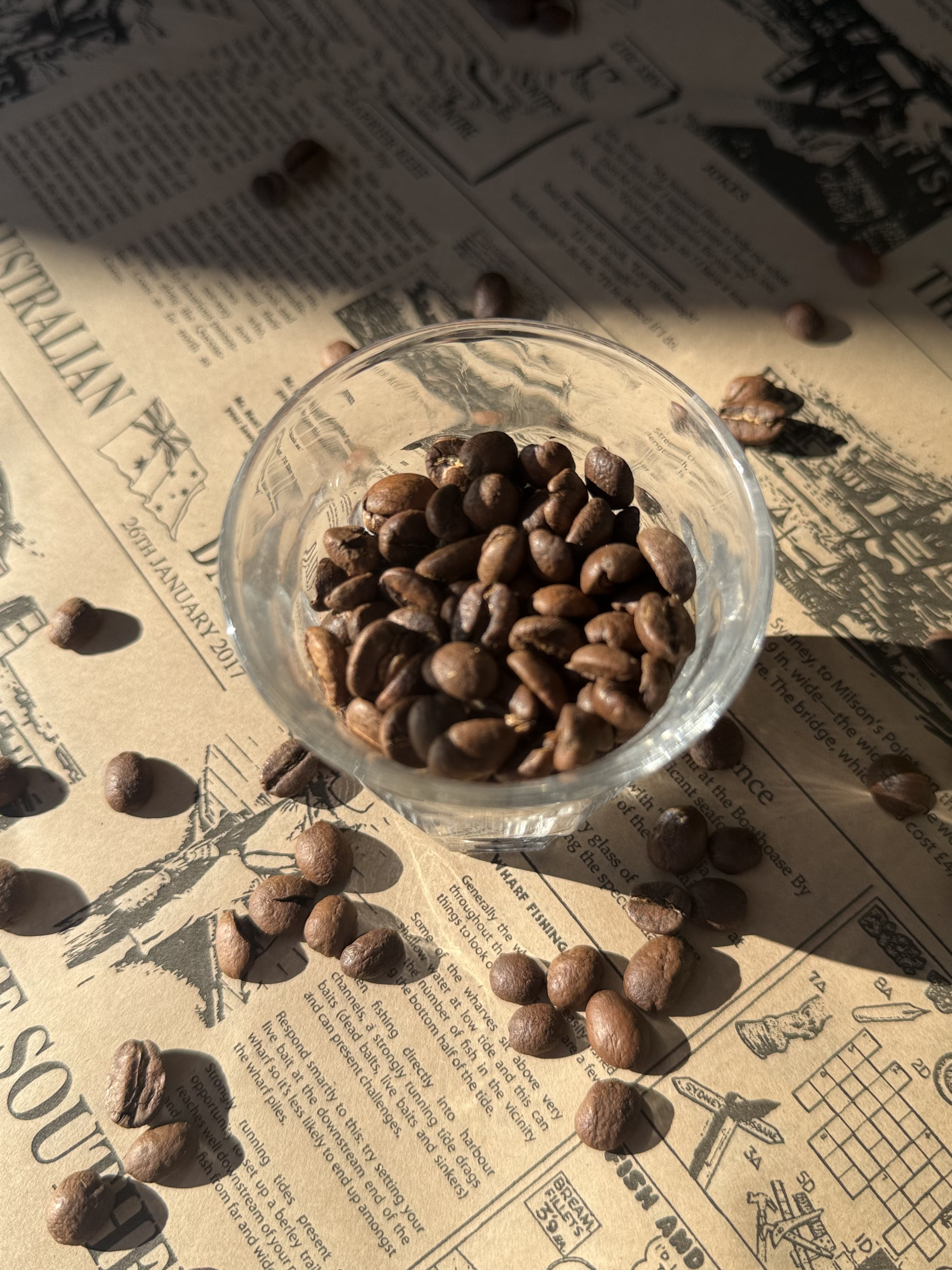Coffee beans in a glass bowl, scattered over a newspaper