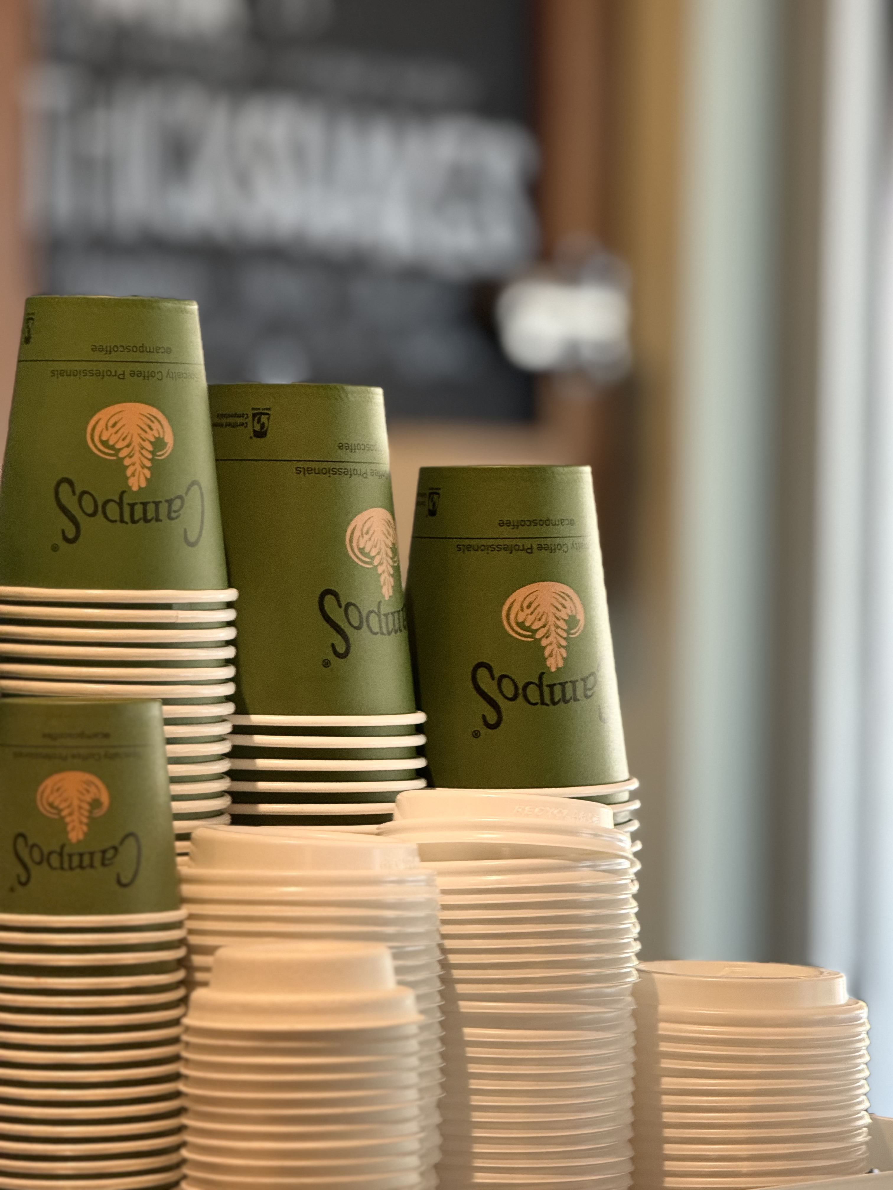 Stacked Campos cups and lids behind the counter